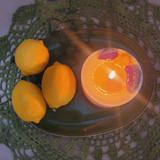 Lit small lemon candle with colorful dried flowers creating warm candlelight ambiance on green ceramic plate