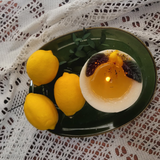 Large lemon candle burning with natural botanicals showing clean wax pool - handmade soy wax candle quality.