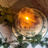 Heart-shaped candle with a warm glow on a decorative plate with greenery