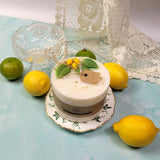 Large lemon scented candle decorated with dried leaves on vintage plate with fresh lemons, limes and pearl necklace
