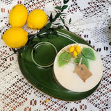 Large lemon candle with botanicals on vintage green serving set with fresh lemons and white lace backdrop