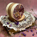 Handmade large pillar soy candle with rose petals decoration displayed on vintage crochet lace and wooden base
