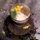 Candle in a glass with lemons decoration and a leaf on a dark surface with flowers.