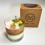 Glass candle with decorative elements and a cardboard box labeled 'BS beauty scents' on a white background.