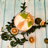 Lemon scented candle decorated with dried citrus slices and mint leaves, surrounded by fresh lemons and limes
