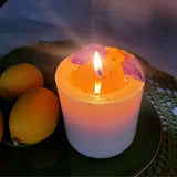 Lit medium lemon scented candle with melted wax pool decorated with dried leaves on antique green ceramic plate