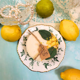 Handmade lemon candle decorated with dried leaves on antique botanical plate with fresh lemons and vintage pearls