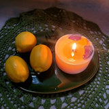 Burning lemon scented candle with dried botanicals on dark green plate with fresh oranges and vintage lace doily