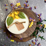 Handmade lemon candle decorated with dried citrus and leaves on wood serving board with scattered dried flowers
