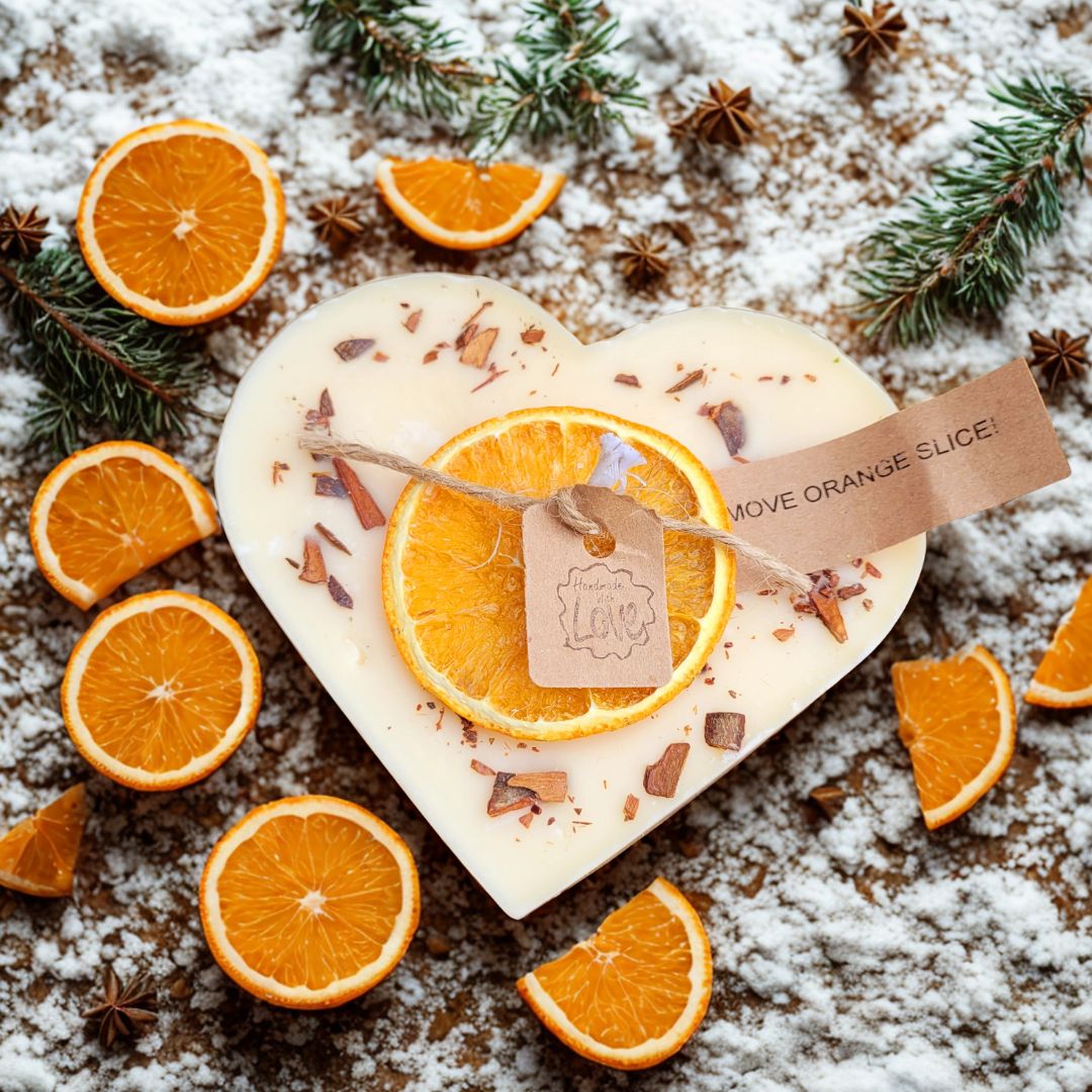 Heart-shaped Orange and Cinnamon soy candle with dried orange slice decoration by Beauty Scents, winter flat-lay with fresh orange slices, star anise, pine branches and snow
