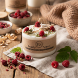 Candle with raspberries on a wooden surface, surrounded by fresh raspberries and leaves.