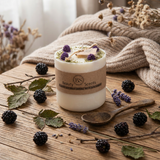 Candle with 'BS Beauty Secret Scents' label on a wooden surface with blackberries and lavender.
