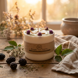 Candle  with a brown label on a wooden surface, surrounded by blackberries and leaves.