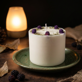 White candle with purple flowers on a green plate with a warm light in the background