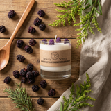 Candle with blackberries and greenery on a wooden surface