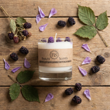 Candle with 'RS Beauty Scents' branding on a wooden surface with blackberries and leaves.