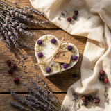 Heart-shaped candle with lavender and berries on a wooden surface, surrounded by more lavender and a beige cloth.