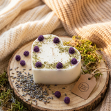 Heart-shaped candle with purple flowers on a wooden surface with lavender and a tag.