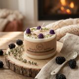 Candle with blackberries and thyme on a wooden board with 'Beauty Scents' branding, fireplace in the background.