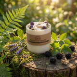 Candle with 'Beauty Secret Scents' label on a wooden stump surrounded by greenery and blackberries