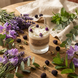Glass candle with floral and greenery arrangement on a wooden surface