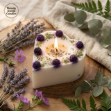 Heart-shaped candle with purple flowers on a wooden surface with lavender and eucalyptus leaves.