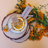 Candle in a glass jar with orange slices and berries on a wooden coaster