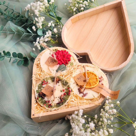 Close-up view of three small heart-shaped winter scented candles showing detailed decorative botanicals and natural soy wax texture