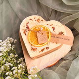 Natural scented heart candle decorated with dried orange and cinnamon by Beauty Scents, styled as gift idea with delicate white flowers and soft textiles