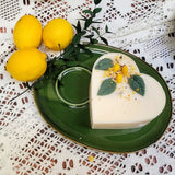 Heart-shaped candle with lemon zest and leaves on a green plate with lemons and greenery.