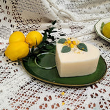 Heart-shaped candle with lemon zest and leaves on a green plate with lemons and greenery.