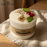 Close-up of a large soy candle with wax cherries and green leaf decoration, with tag and label, styled on beige cloth on a wooden table.