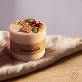 Large soy candle with wax cherries and green leaf decoration, with tag and label, on beige cloth on a wooden table in warm sunset light.