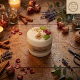 Large soy candle with wax cherries and green leaf decoration, with tag and label, styled on a rustic wooden table with candlelight, dried rose petals, lavender, cinnamon sticks and greenery.
