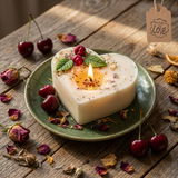 Beauty Scents Heart-shaped candle with wax cherries and green  leaf lit on a green plate and wooden surface. Sun light. top view.