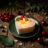 Beauty Scents Heart-shaped candle with wax cherries and green  leaf lit on a green plate and wooden surface. Night light. Top view.