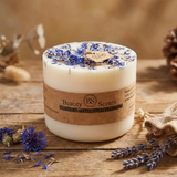 Candle with dried flowers on top, branded 'Beauty Scents', on a wooden surface with lavender and cornflowers.
