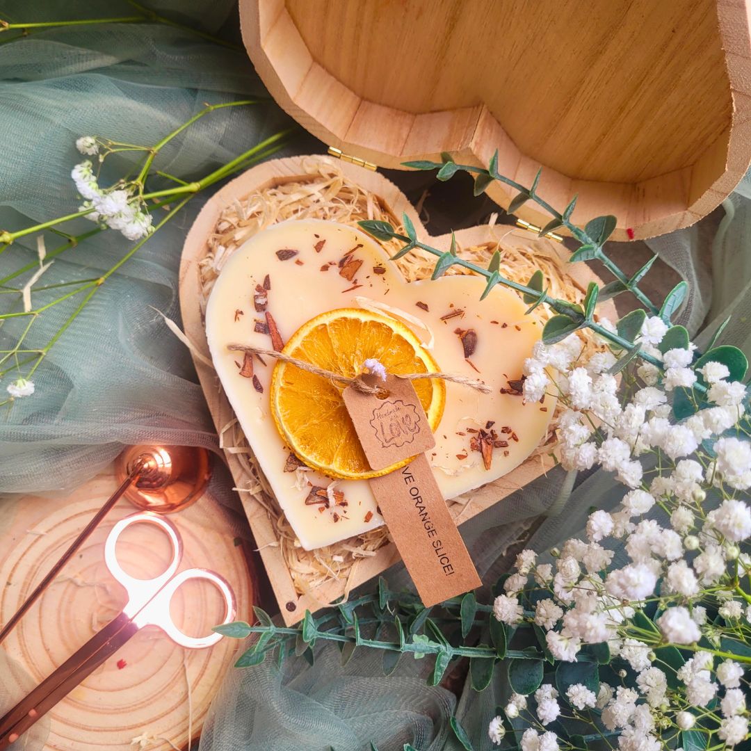 Large heart-shaped orange and cinnamon scented candle with detailed view of dried orange slices and cinnamon stick decorations