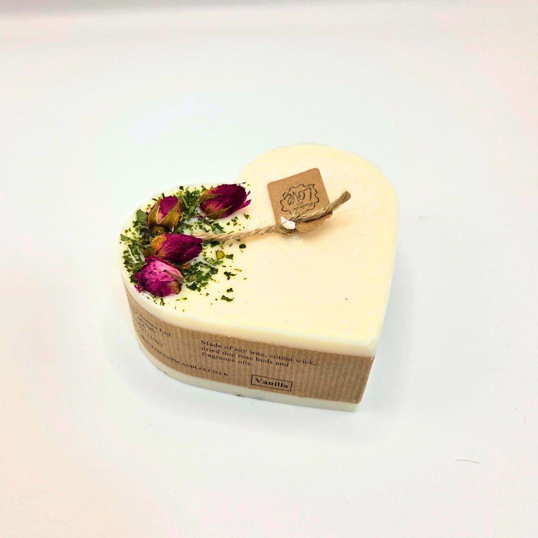 Heart-shaped candle with dried flowers and a tag on a white background