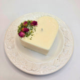 Heart-shaped white candle with dried roses on a decorative plate