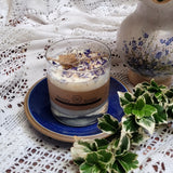 Large Glass Wild Flowers soy candle 800g in clear glass container with blue cornflowers decoration and Beauty Scents label on blue ceramic plate, styled with white lace doilies, floral vase and fresh variegated foliage - large glass container lifestyle photography