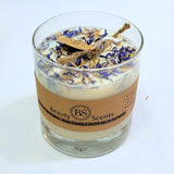 Candle in a glass jar with wildflower petals and a brown label on a white background