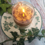 Large Glass Wild Flowers soy candle 800g burning with lit flame and Beauty Scents label in clear glass container, blue cornflowers floating in melted wax pool, styled on ivy-patterned plate with fresh ivy - large glass container burning ambiance photography