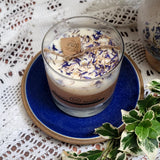 Glass candle with decorative elements on a blue coaster on a lace tablecloth