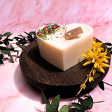 Heart-shaped candle on a wooden stand with flowers and greenery on a pink background