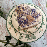 Large Heart Wild Flowers soy candle 500g with blue cornflowers decoration and Beauty Scents label on ivy-patterned plate, styled with fresh ivy leaves and white lace - heart-shaped rustic botanical lifestyle photography