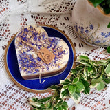 Large Heart Wild Flowers soy candle 500g with blue cornflowers decoration and branded tag on blue ceramic plate, styled with floral vase and fresh variegated foliage - romantic heart-shaped vintage lifestyle photography