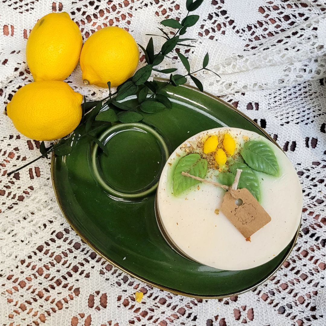 Large lemon candle with botanicals on vintage green serving set with fresh lemons and white lace backdrop
