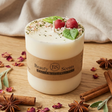 Medium soy candle with cherry wax melt decoration on a wooden table, styled with cinnamon sticks, star anise, eucalyptus leaves and dried petals, with beige textile backdrop. Close up