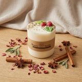 Medium soy candle with cherry wax melt decoration on a wooden table, styled with cinnamon sticks, star anise, eucalyptus leaves and dried petals, with beige textile backdrop